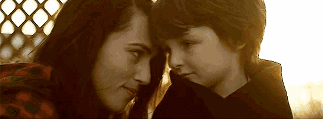 a woman and a boy are looking at each other with a fence in the background