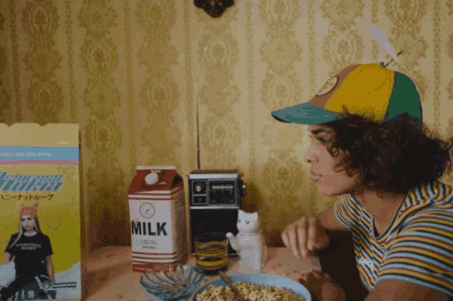 a person sitting at a table with a carton of milk and a box of cereal