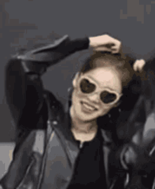 a woman wearing sunglasses and a leather jacket is dancing with her arms in the air .