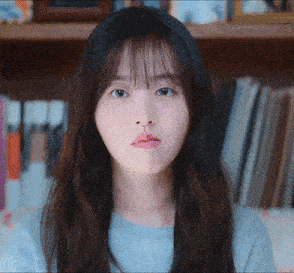 a close up of a woman 's face with a bookshelf behind her