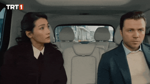 a man and a woman are sitting in the back seat of a car with trt1 on the bottom left