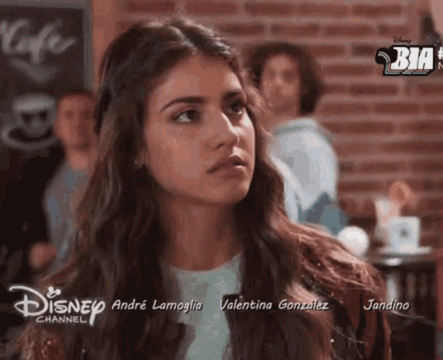 a woman is sitting at a table in front of a brick wall and a sign that says disney channel