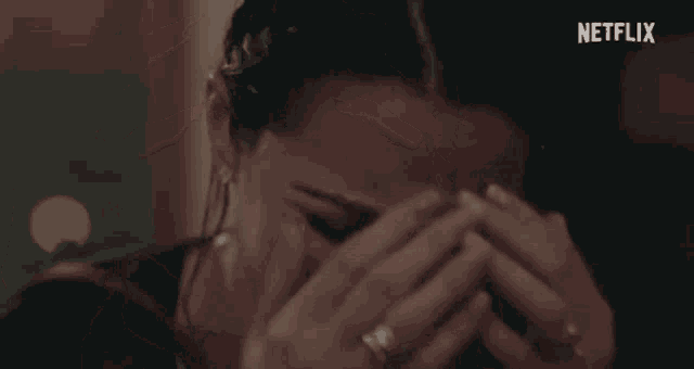 a close up of a woman covering her face with her hands with a netflix logo in the background