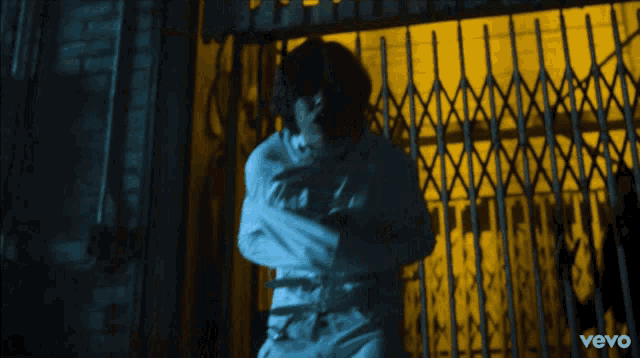 a man in a straitjacket is standing in front of a yellow gate with the word vevo on the bottom right