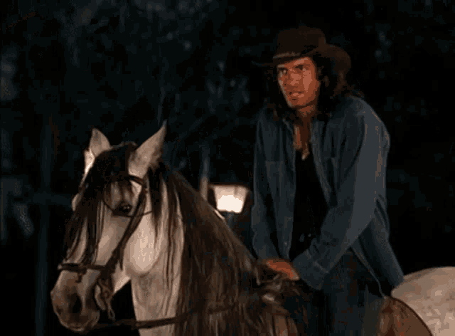 a man wearing a cowboy hat is standing next to a white horse .