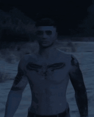 a shirtless man with a tattoo on his chest is standing in the dark