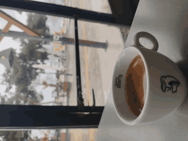 a cup of coffee from alberto sits on a table in front of a window