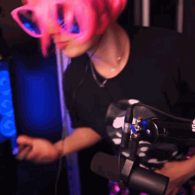 a person wearing pink hair and glasses is standing in front of a rode microphone