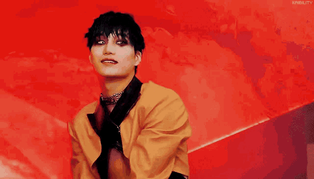 a man wearing a yellow jacket and black tie looks at the camera with a red background behind him that says kinquity