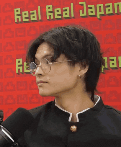 a man wearing glasses and earrings stands in front of a sign that says real real japan