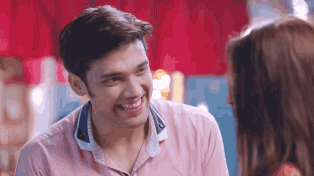 a man and a woman are looking at each other and smiling . the man is wearing a pink shirt .