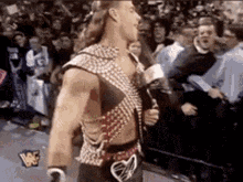a man in a wrestling outfit is walking in front of a crowd holding a microphone .