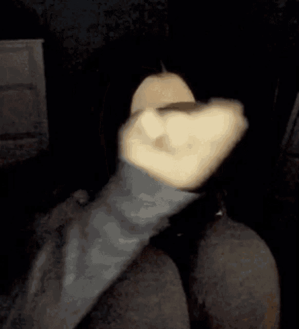 a person is covering their face with their hand in a dark room in a blurry photo .