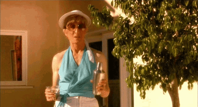 a woman wearing a hat and sunglasses holds a martini and a bottle