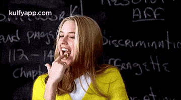 a woman in a yellow shirt is laughing in front of a blackboard with the word discrimination written on it