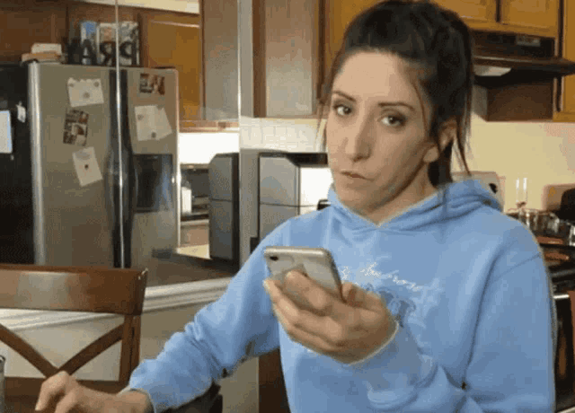 a woman in a blue sweatshirt holds a cell phone in her hand