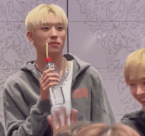 a man with blonde hair is drinking from a bottle with a straw in his mouth
