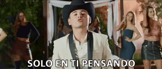 a man in a cowboy hat is standing in front of a group of women and the words solo en ti pensando are above him .