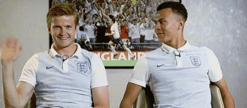 two soccer players are sitting next to each other in front of a poster that says england .
