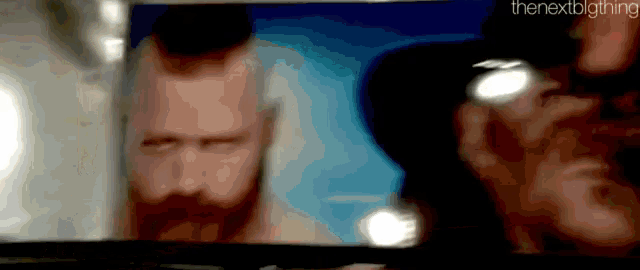 a man with a beard is looking at another man with sunglasses on a television screen .