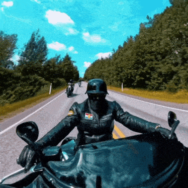 a person wearing a harley davidson jacket is riding a motorcycle down a road