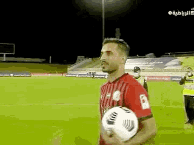 a man in a red and black striped shirt is holding a soccer ball on a field .