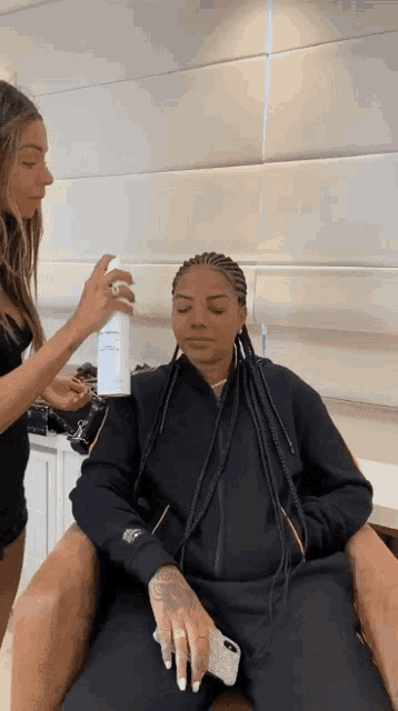 a woman with braids is getting her hair sprayed by a woman in a black jacket