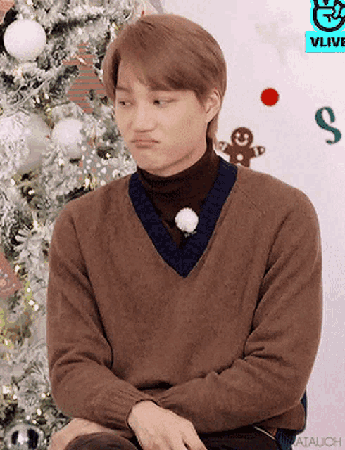 a man wearing a brown sweater is sitting in front of a christmas tree ..