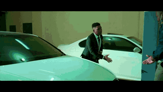 a man in a suit and tie is standing between two cars