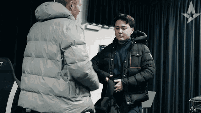a man in a grey jacket is helping another man in a black jacket