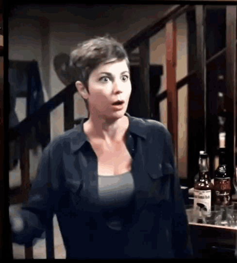 a woman in a black shirt is standing in front of a staircase with a bottle of whiskey in the background
