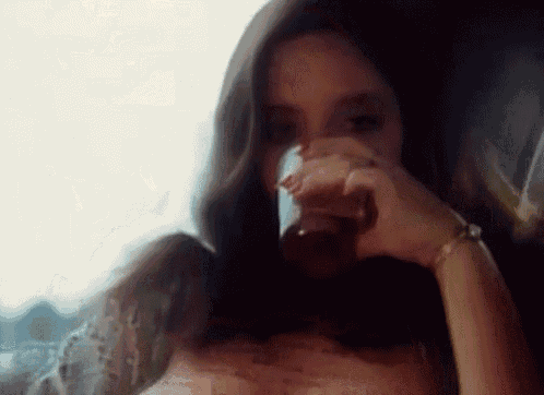 a woman is drinking a glass of wine while sitting in front of a window .