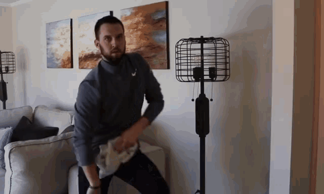 a man in a grey shirt is standing in a living room with a lamp