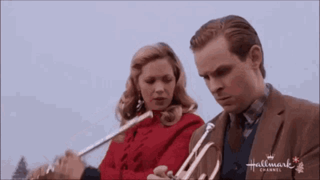 a man and a woman are standing next to each other playing trumpets .