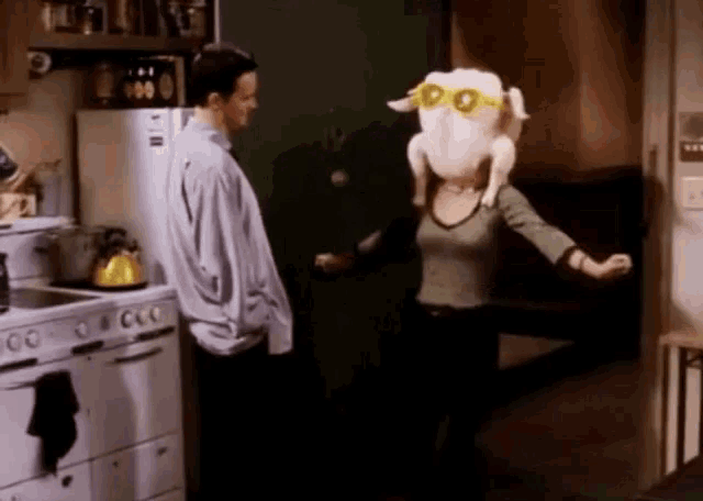 a man and a woman in a kitchen with a stuffed turkey on their head .
