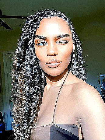 a woman with long curly hair is taking a selfie in a room with a ceiling fan in the background .