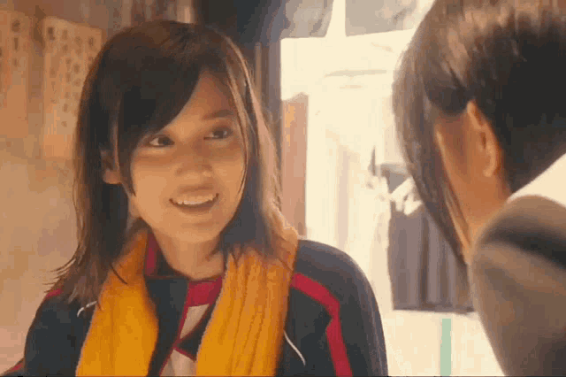 a woman with a yellow scarf around her neck smiles while talking to another woman