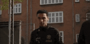 a man wearing a black jacket is standing in front of a brick building .