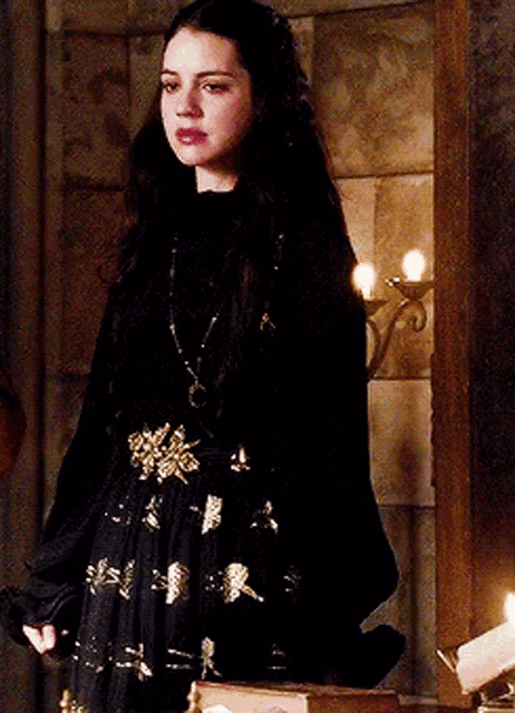 a woman in a black dress is standing in a room with candles and a book .