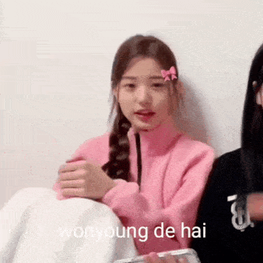 a girl in a pink sweater is sitting next to a girl in a black sweater .