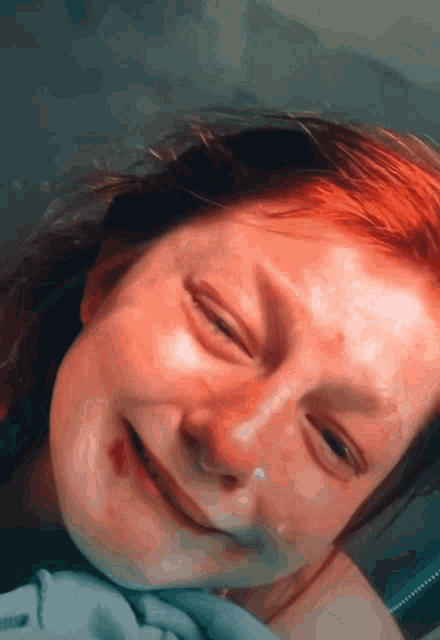 a young girl with red hair is smiling with a tear coming out of her nose