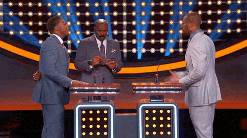 three men in suits are standing in front of microphones on a stage talking to each other .