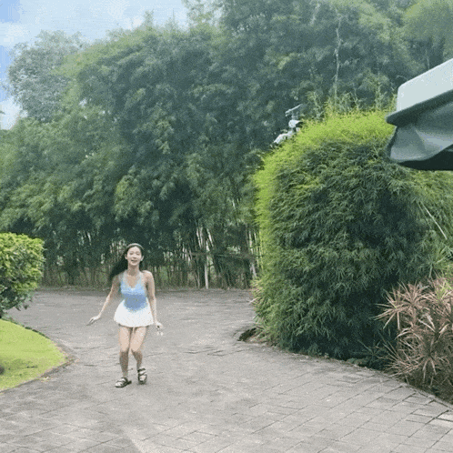 a woman in a blue tank top and white skirt is walking down a brick road