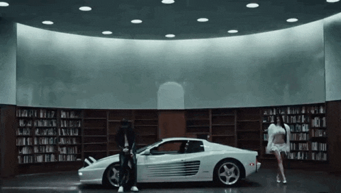 a man and a woman are standing next to a white car in a library
