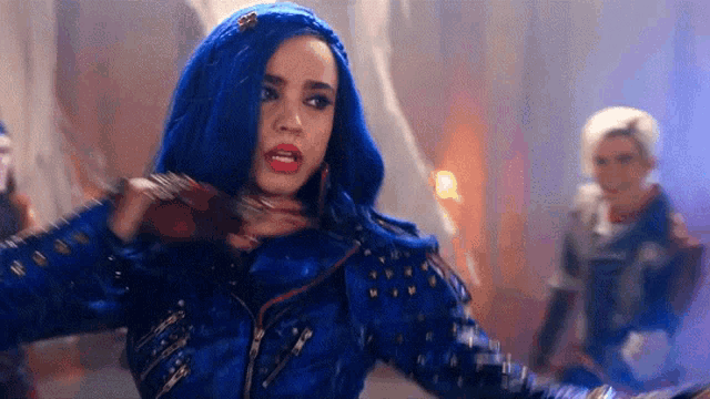 a woman with blue hair and a blue jacket is standing in a dark room with other people .