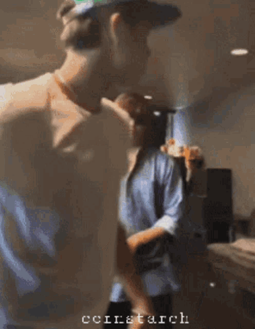 two men are standing next to each other in a room and one of them is wearing a hat and sunglasses .