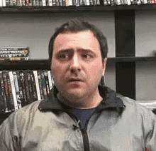 a man in a jacket stands in front of a shelf of dvds