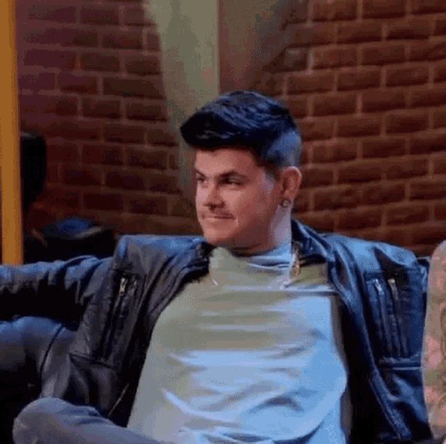 a young man is sitting on a couch wearing a leather jacket .