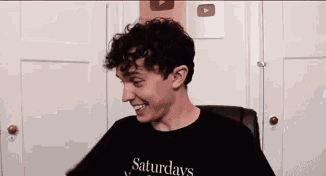 a young man with curly hair is sitting in a chair and smiling .