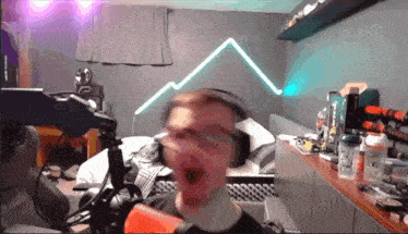 a man wearing headphones is sitting in front of a microphone in a bedroom with a mountain in the background .